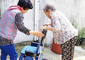보조기구를 사용하여 걷고 있는 할머니를 요양사가 도와주고 있는 사진